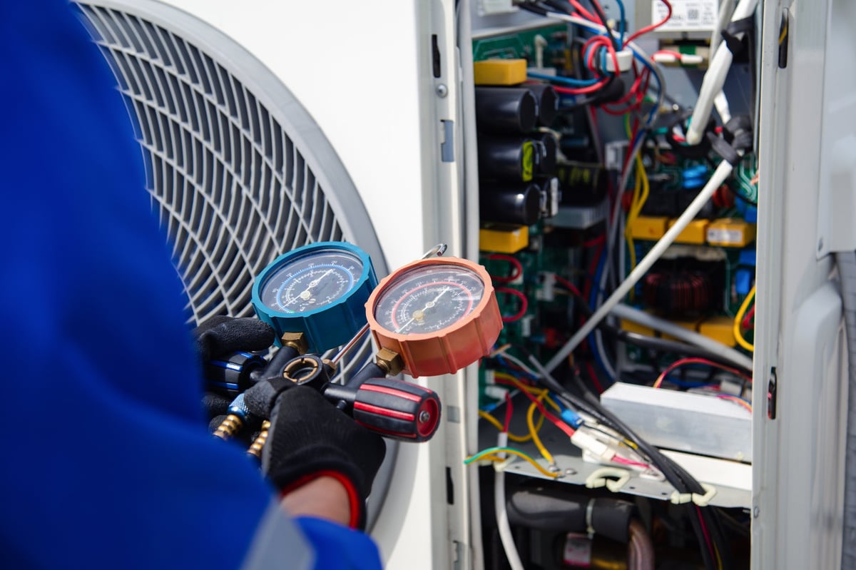 Technician using a gauge to measure refrigerant pressure during air conditioner service