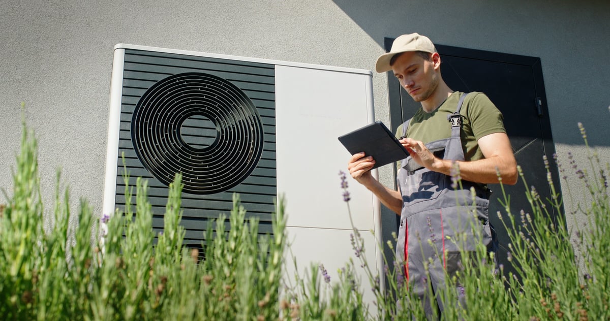 Technician inspecting an outdoor heat pump unit using a tablet on a sunny day